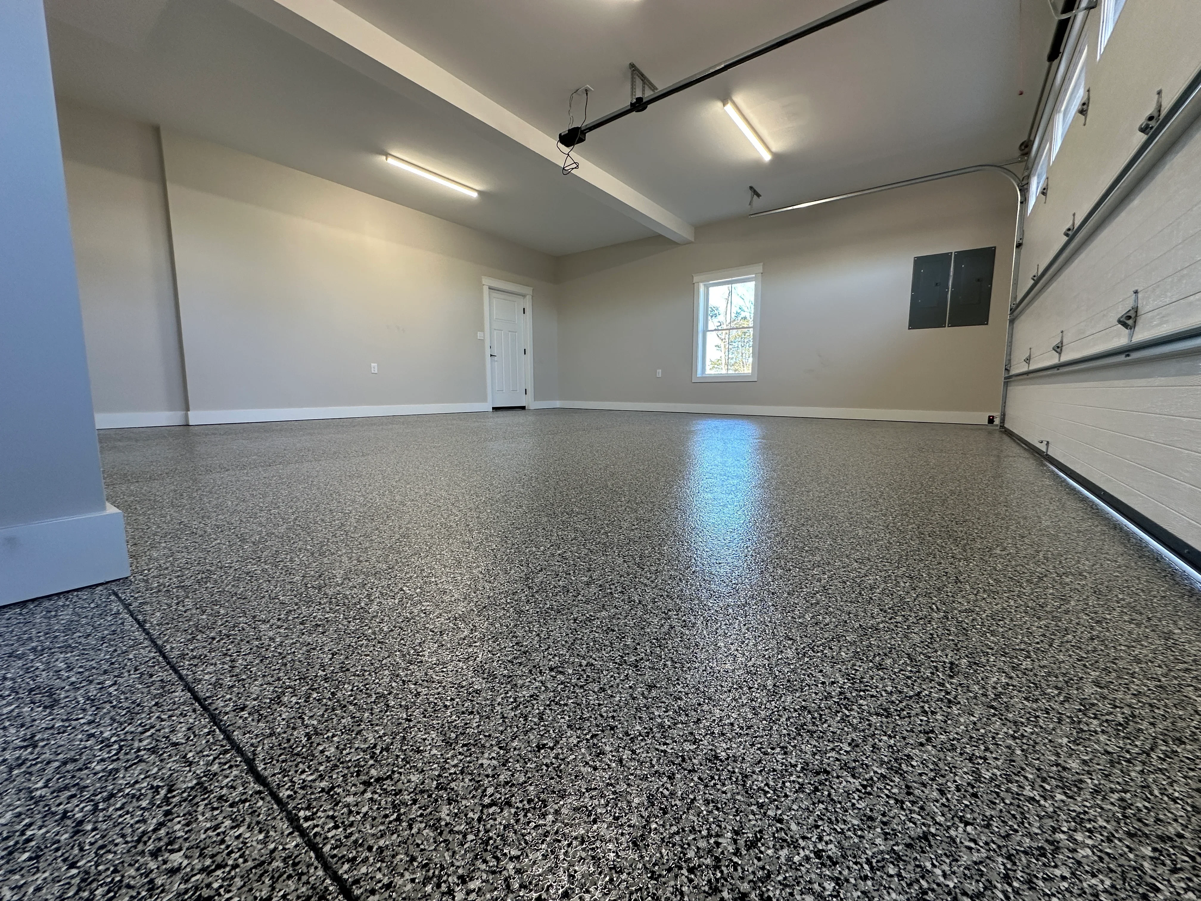 Polished gray epoxy-coated garage floor with black control joints and recessed lighting