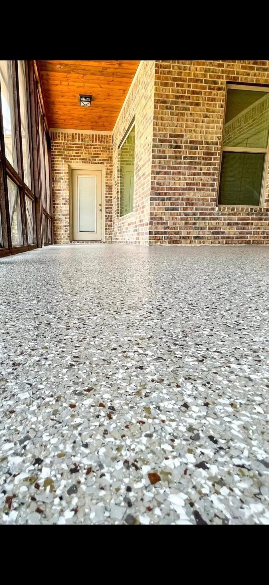 Polished aggregate concrete coating with white and tan stone chips on covered patio with brick walls