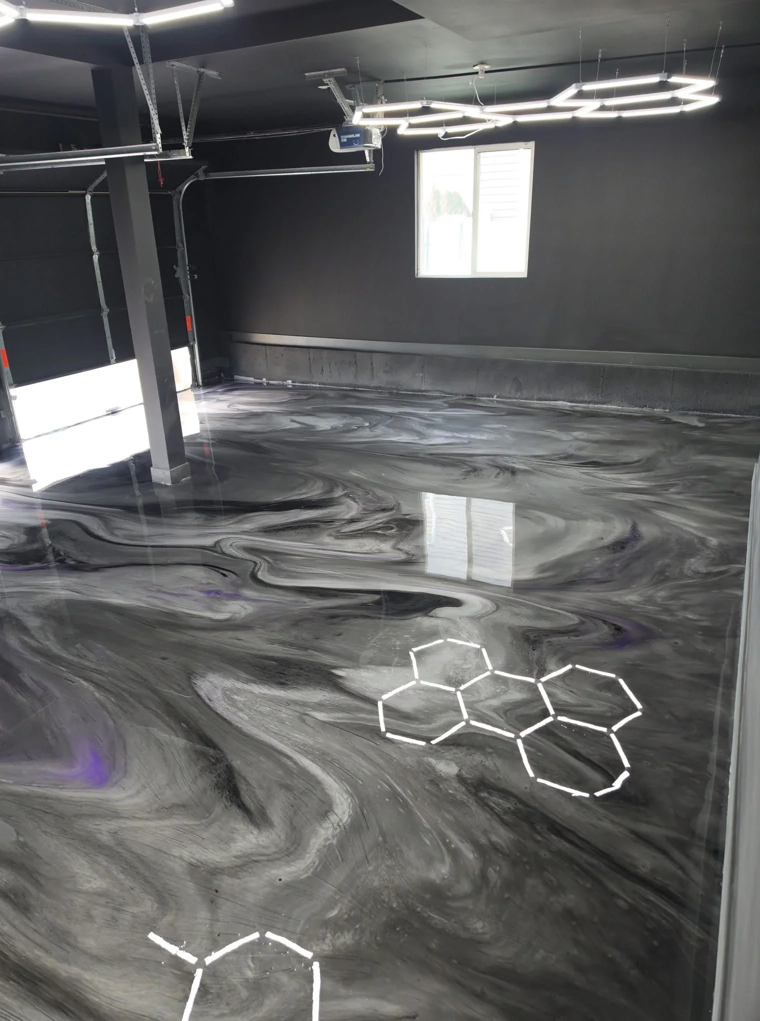 Metallic epoxy garage floor with swirled gray and black patterns, reflective finish, LED lighting overhead
