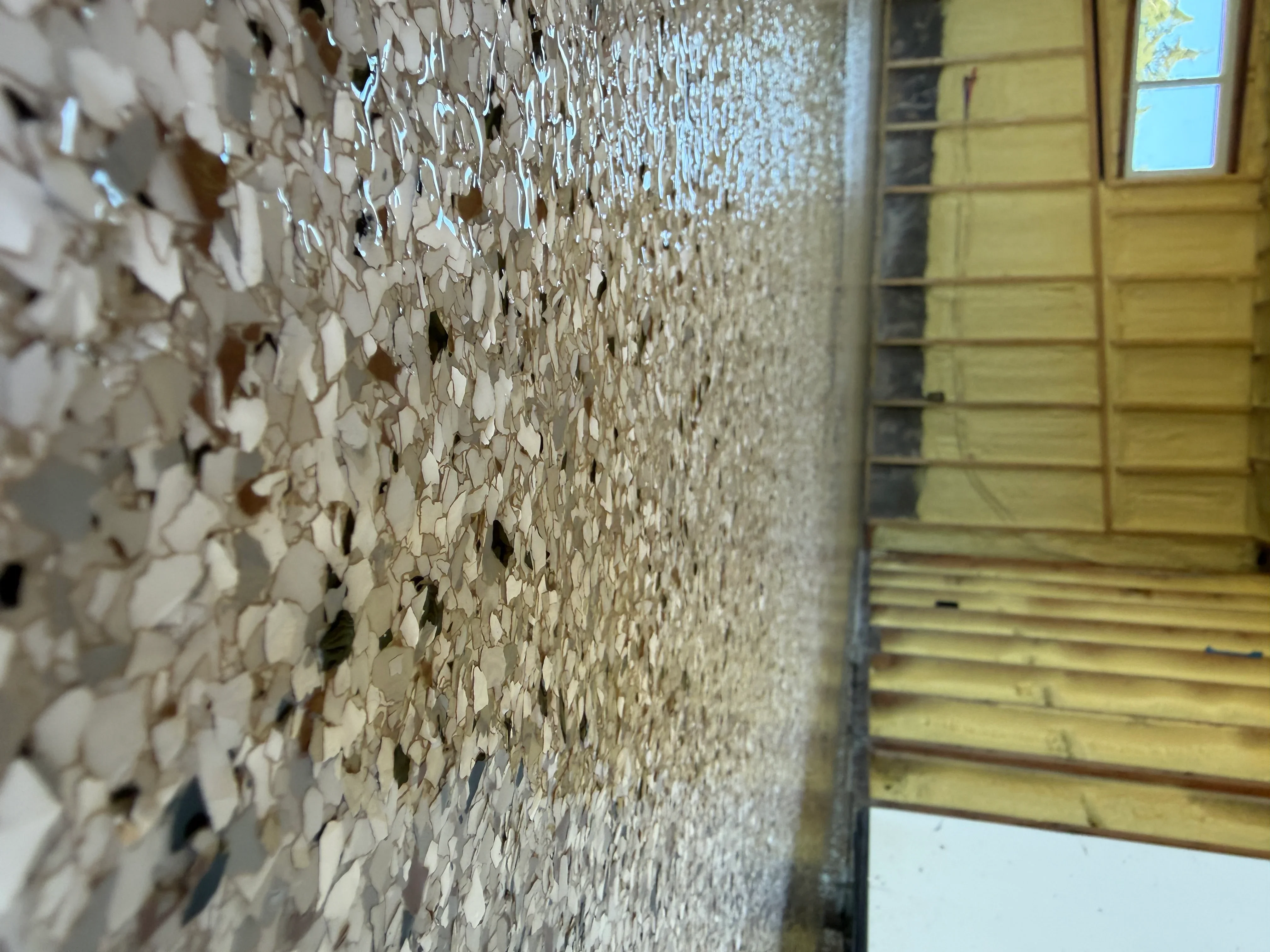 Speckled epoxy garage floor coating with neutral and brown flecks, adjacent to yellow garage doors