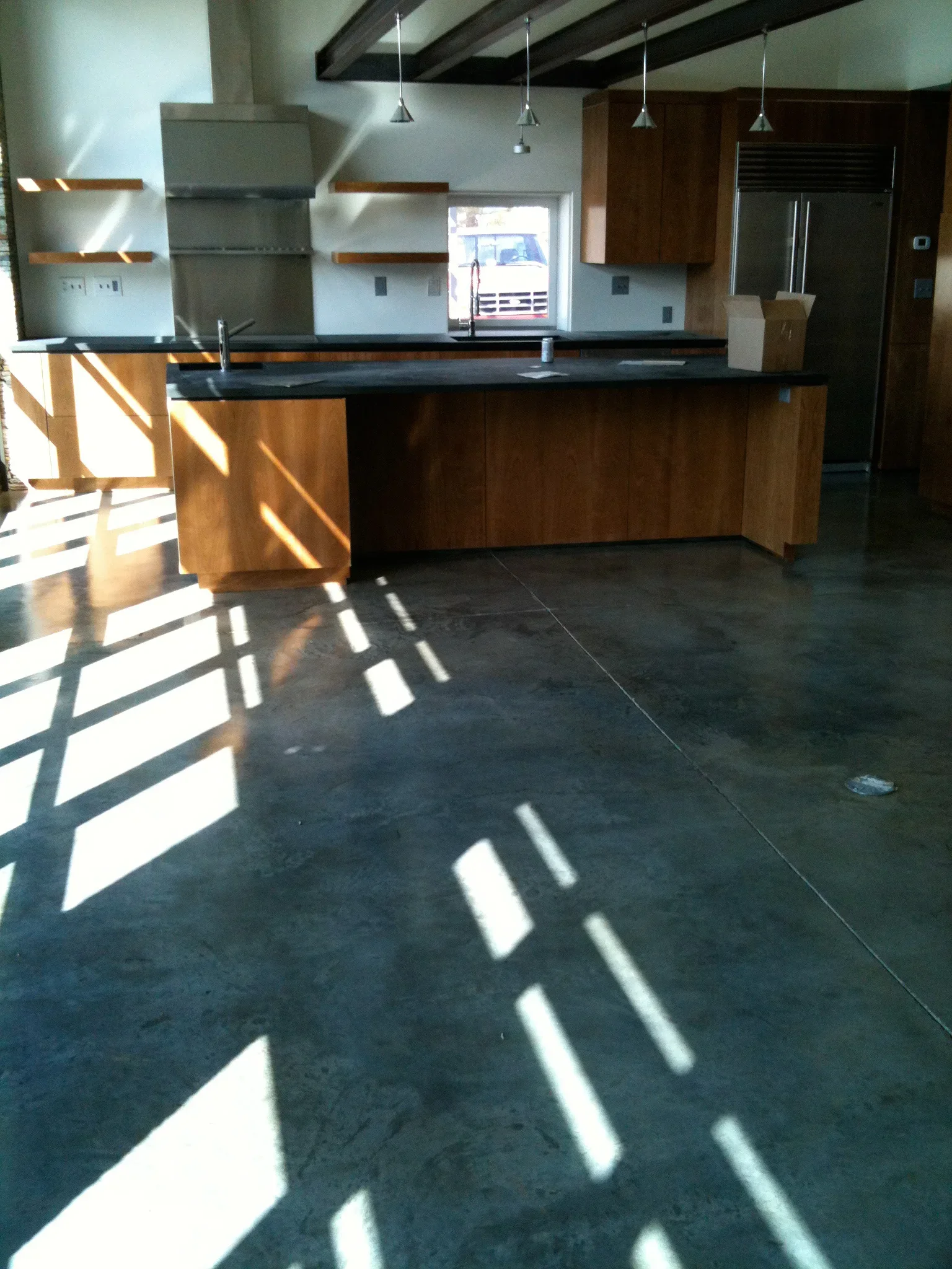 Polished dark concrete floor in modern kitchen with wood cabinets and black countertops