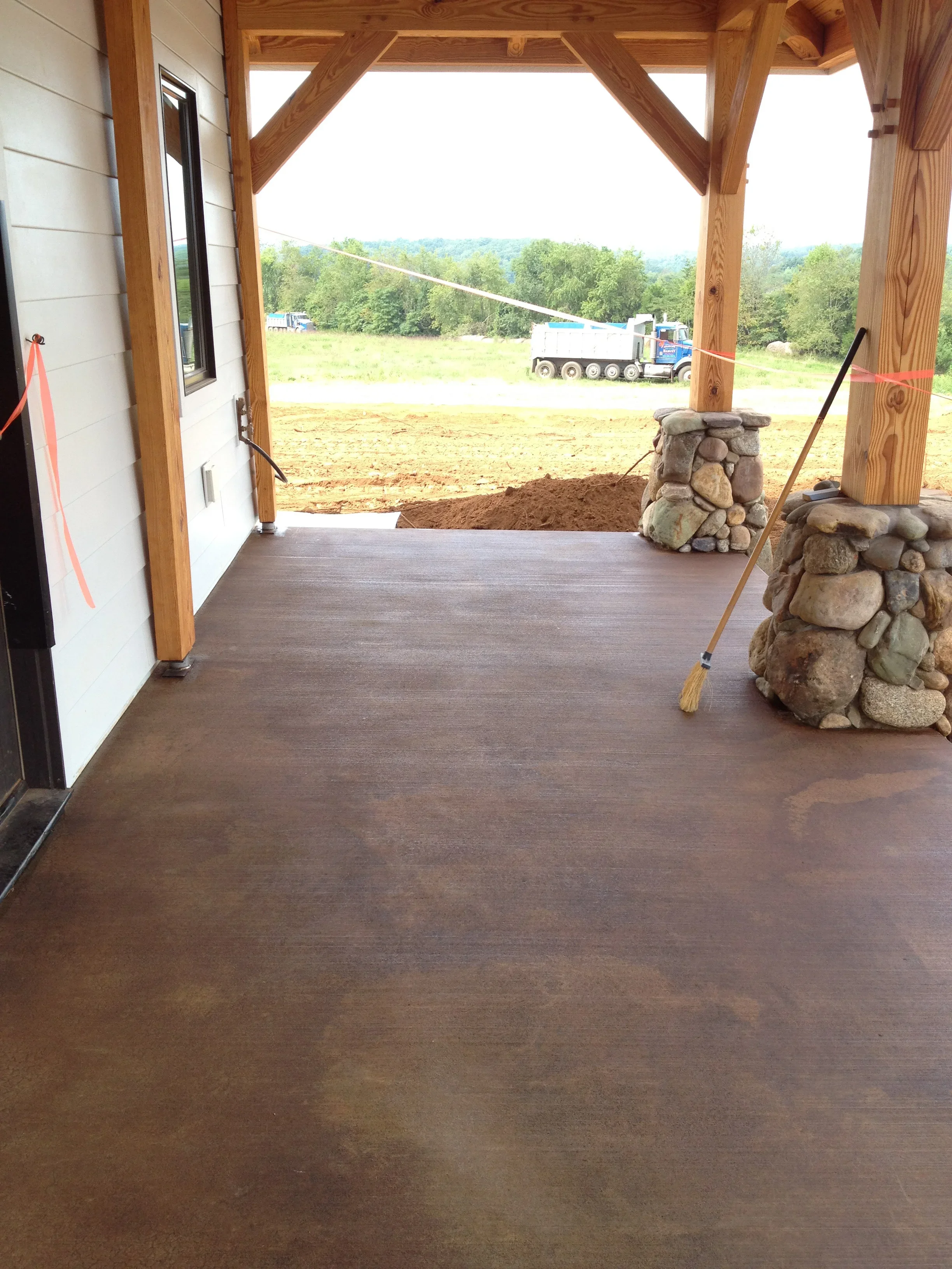 Brown stained concrete porch floor with timber frame structure and stone chimney elements