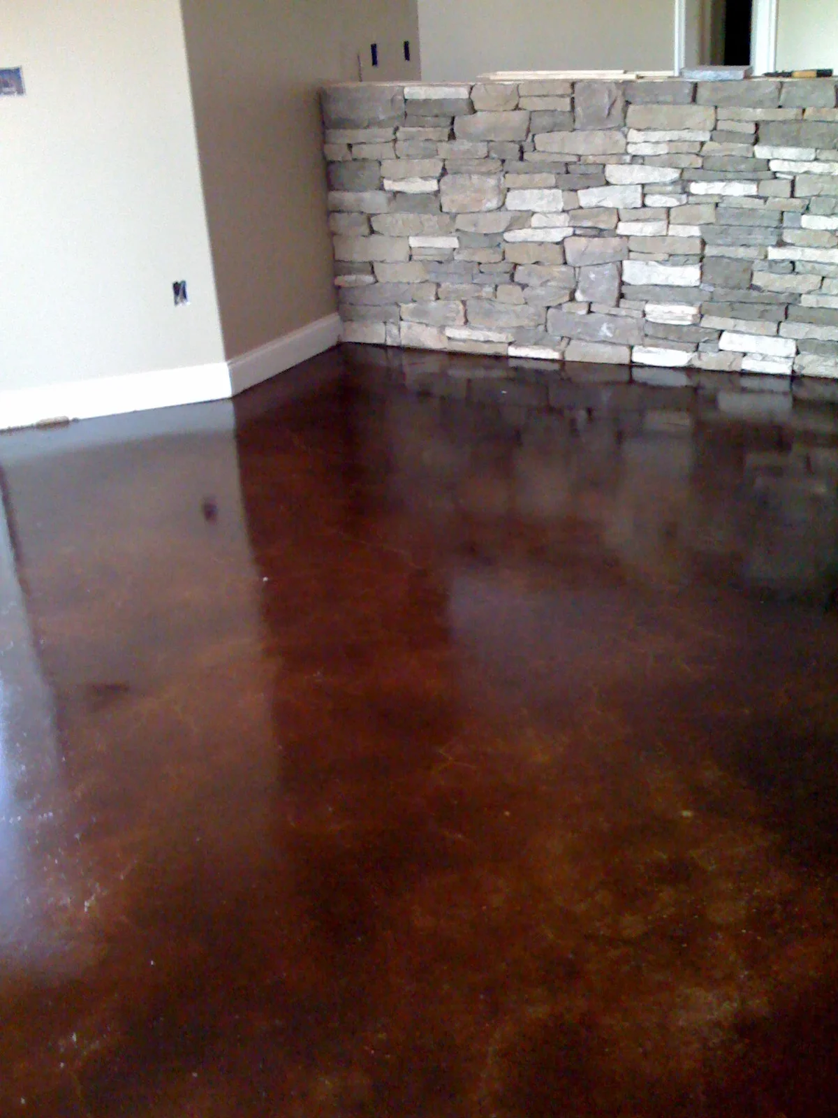 Dark brown concrete floor coating with mottled finish in interior room with exposed brick wall