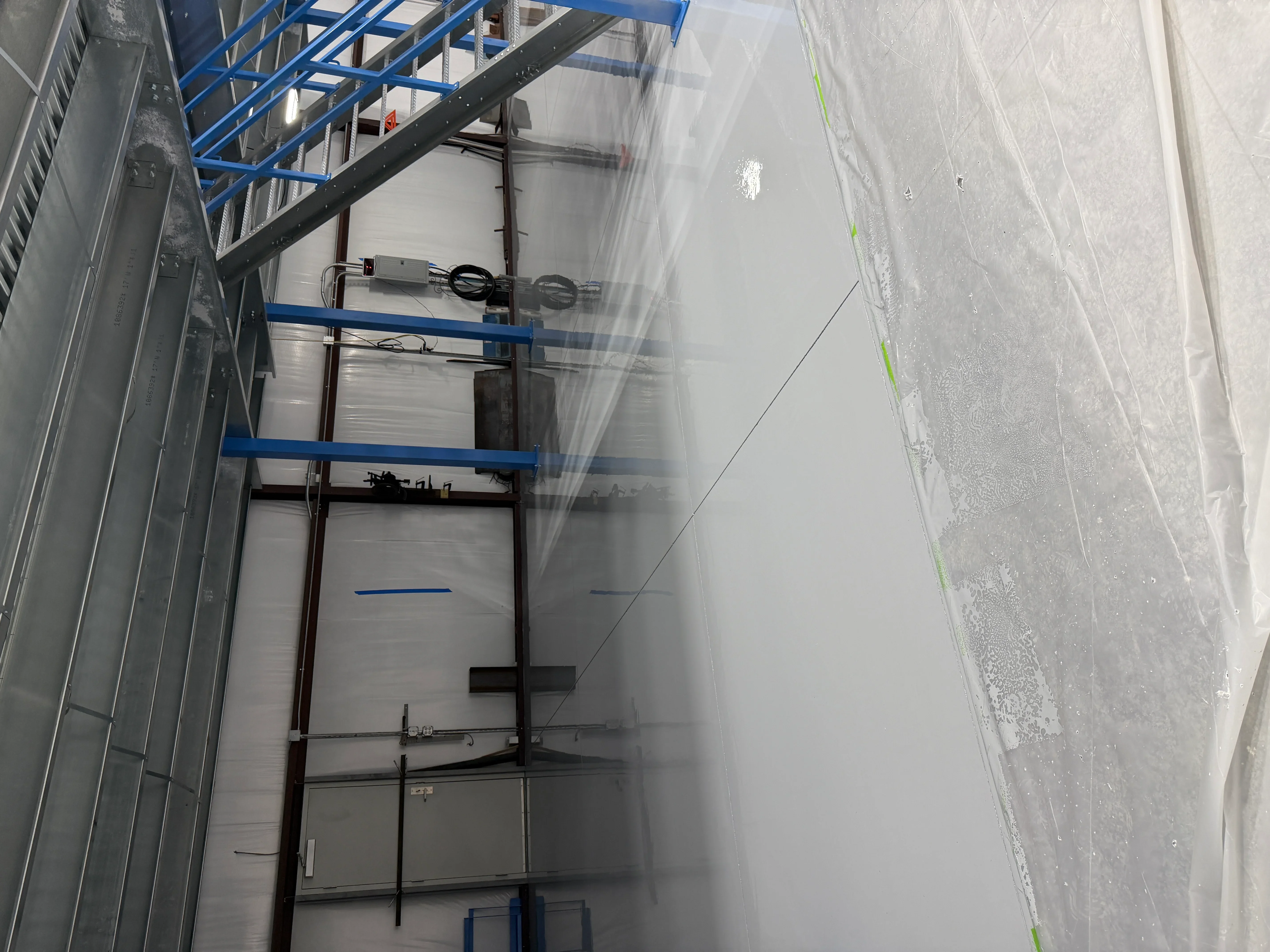 Industrial concrete floor with fresh epoxy coating, metal scaffolding, and protective plastic sheeting during installation