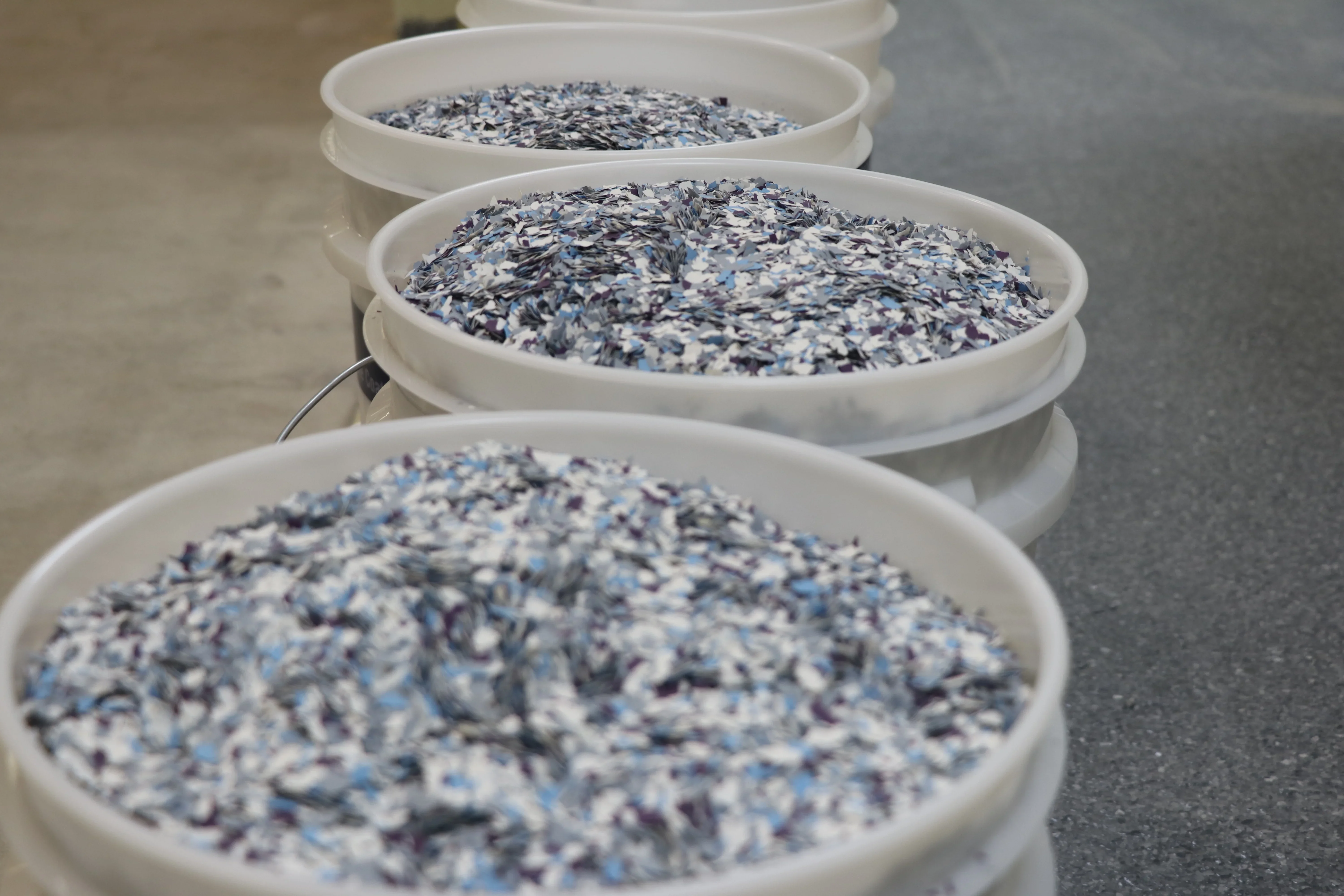Four white trays with blue, white, and charcoal decorative concrete coating flake samples